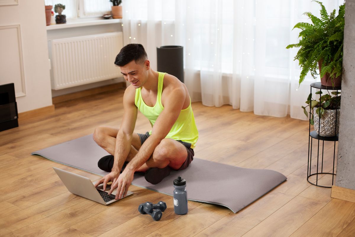 fitness man sitting on a mat and writing on laptop
